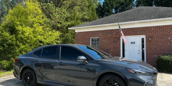 A dark gray sedan parked in front of Atlantic Tint & Wraps, showcasing a professional paint protection film (PPF) application and window tinting.